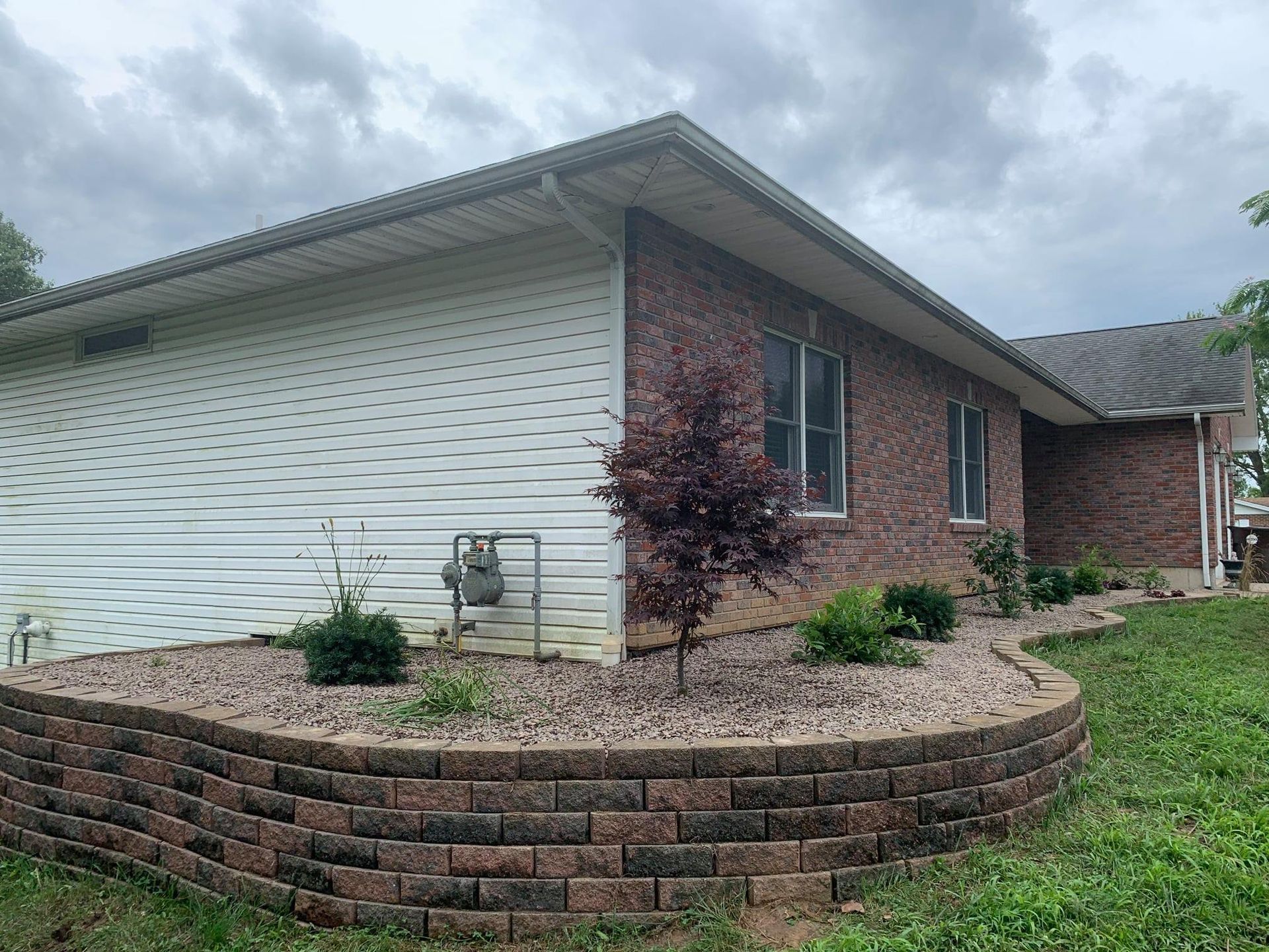 A brick and siding house with a curved retaining wall and landscaped flower bed in the front yard.