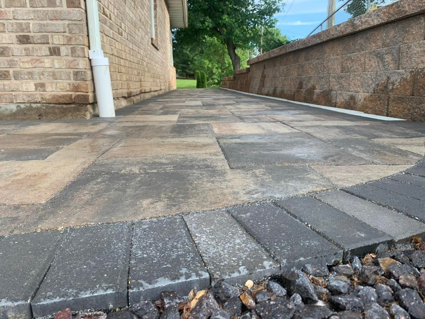 A low-angle view of a new stone paver walkway next to a brick house and a stone retaining wall.