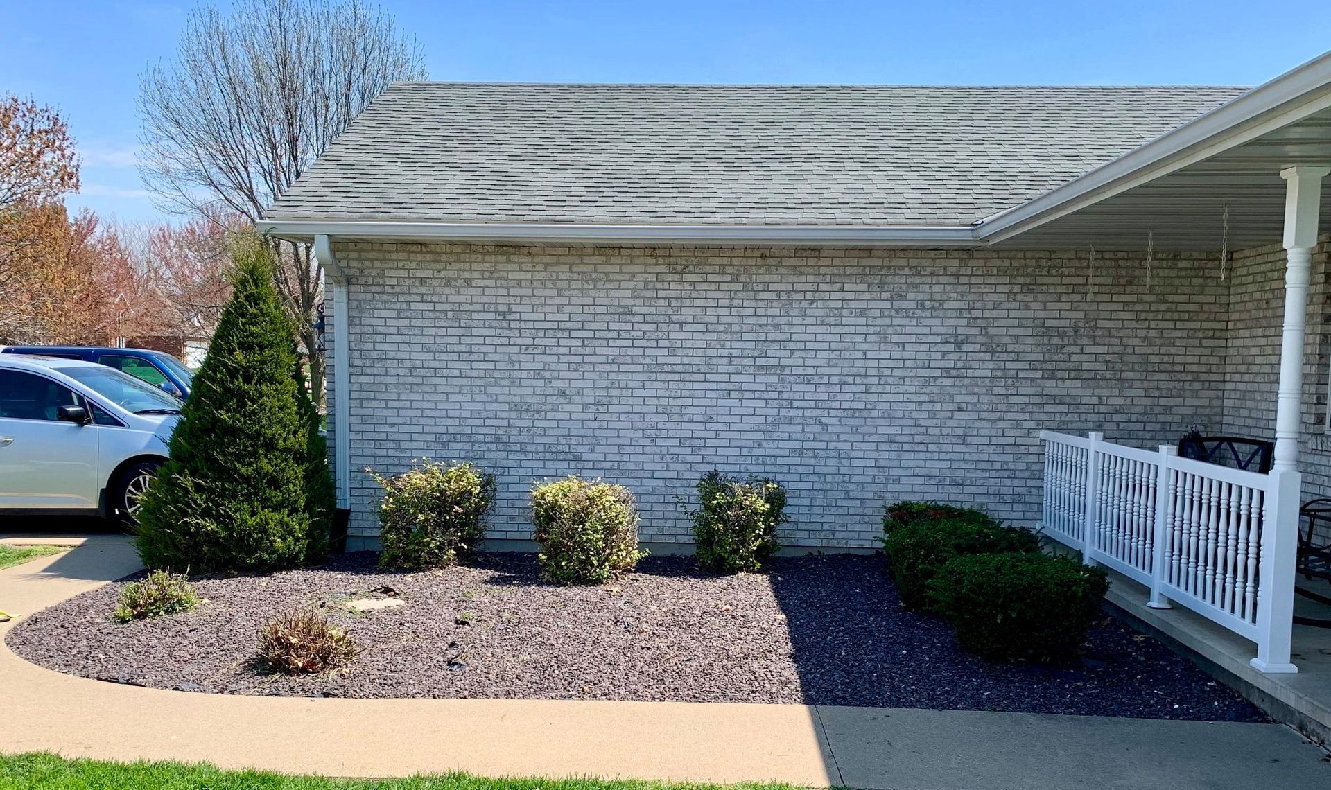 A front exterior view of a house with white brick walls, a dark grey gravel landscaping bed, and small green shrubs.