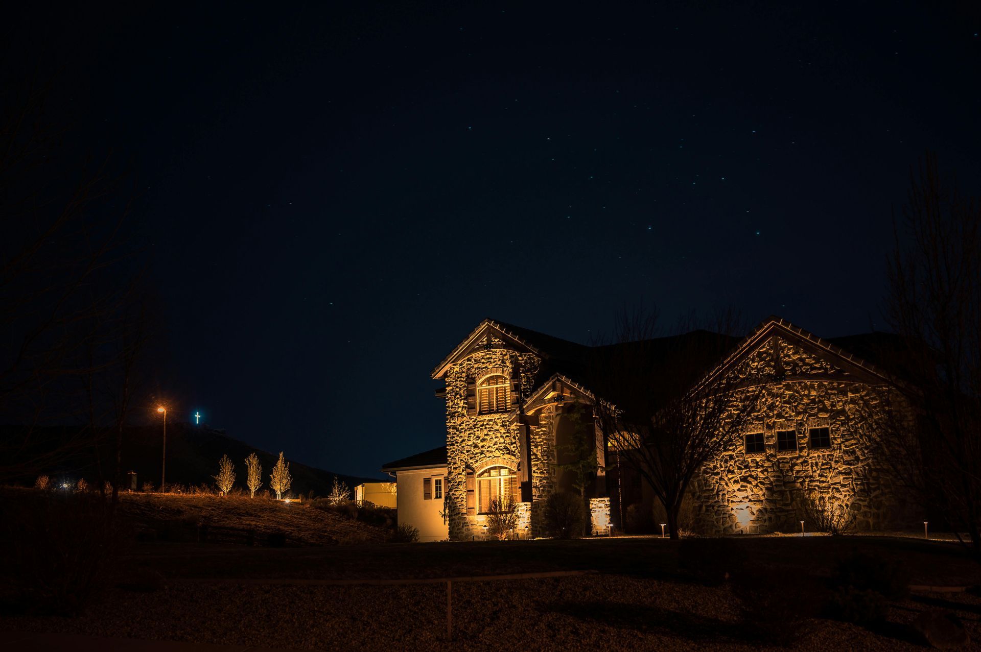 A two-story stone house illuminated by warm exterior accent lighting against a dark, starry night sky.