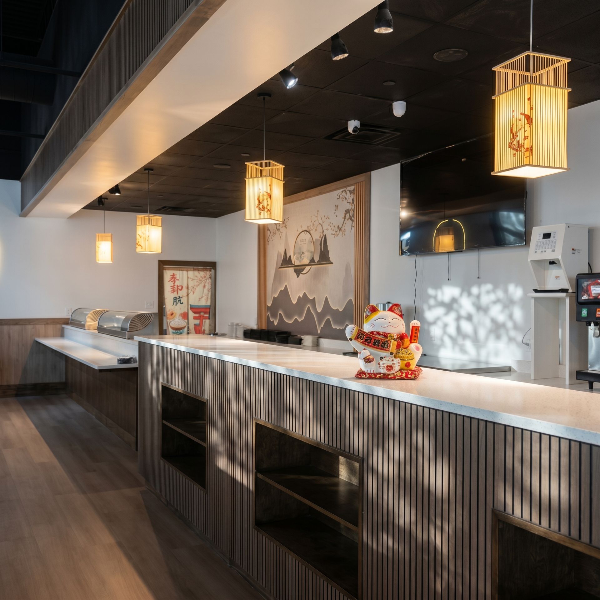 Modern restaurant bar with hanging lanterns, dark wood counters, and a sushi display in a sleek interior