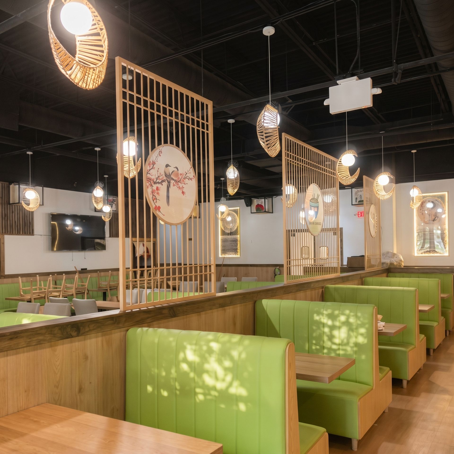Modern restaurant interior with green booths, wood accents, hanging lights, and decorative room dividers