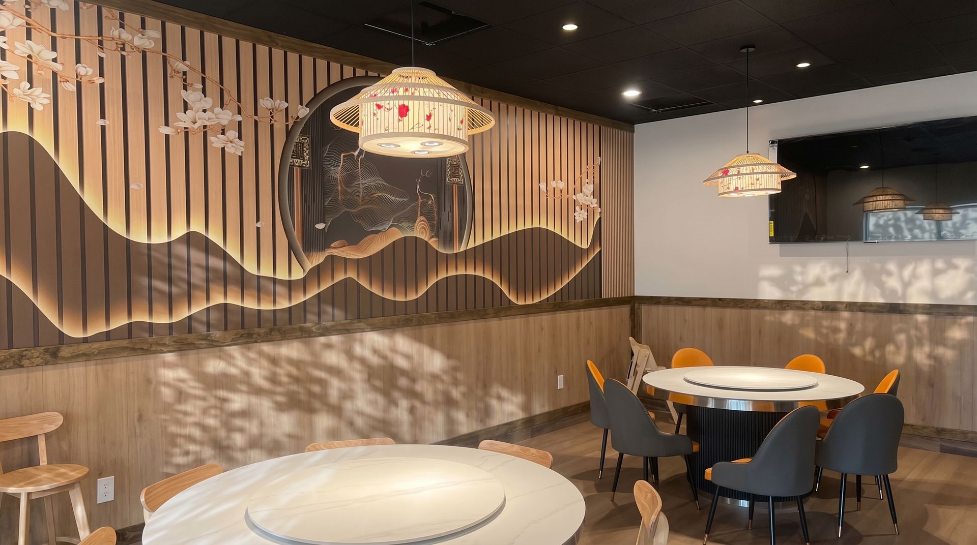 Modern restaurant interior with wooden wall art, hanging lights, and round tables with chairs
