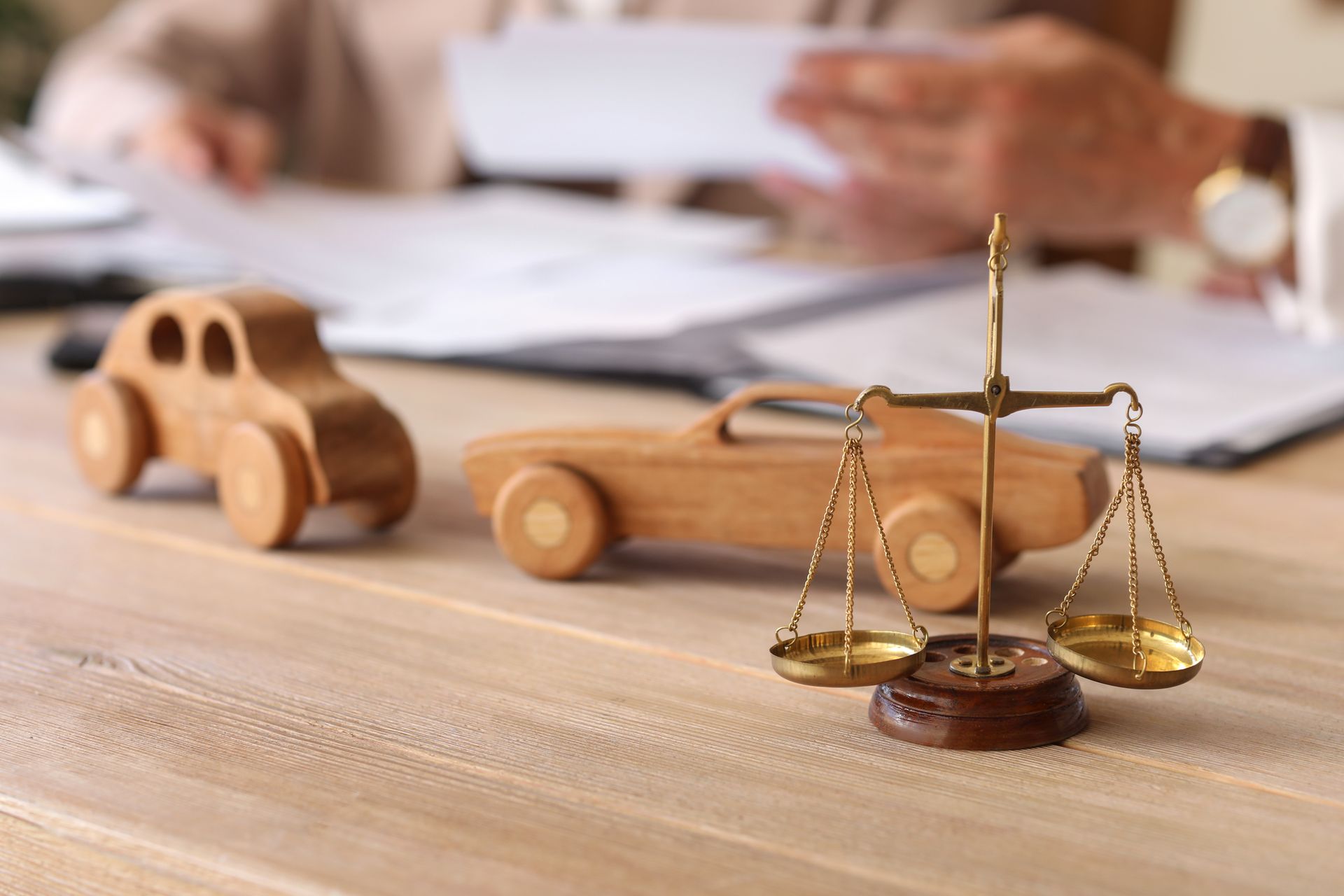 Scale of justice beside wooden toy cars on a desk, symbolizing legal claims after vehicle accidents.