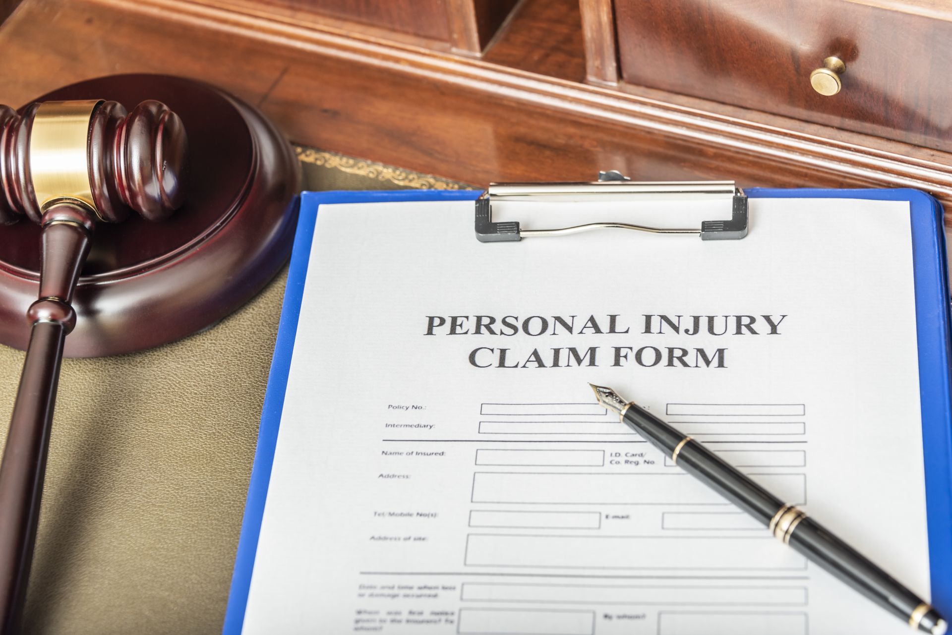 Gavel and pen next to a personal injury claim form on a wooden desk. Gavel and pen next to a personal injury claim form on a wooden desk.