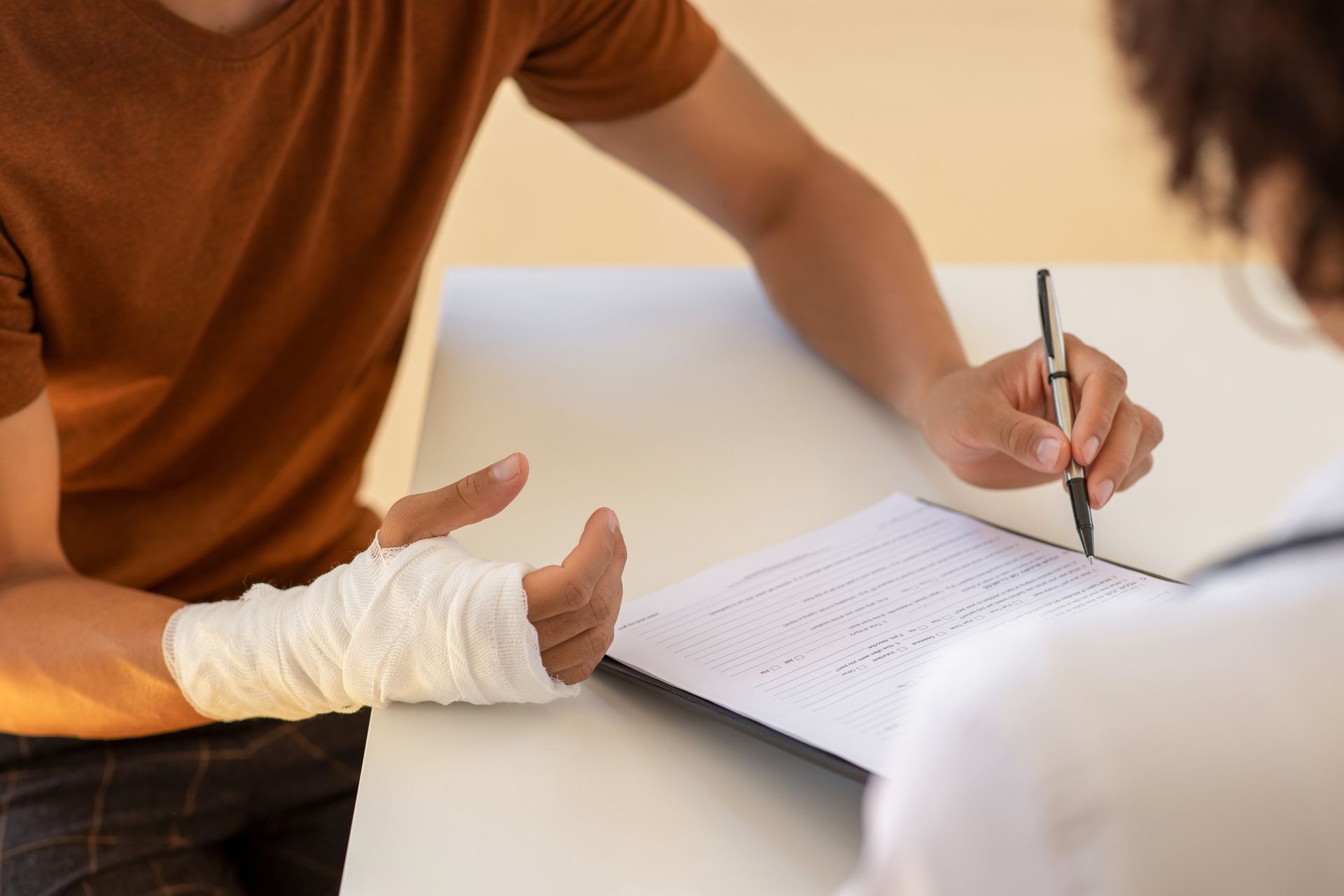 Person with bandaged hand fills out form with assistance at a table. 