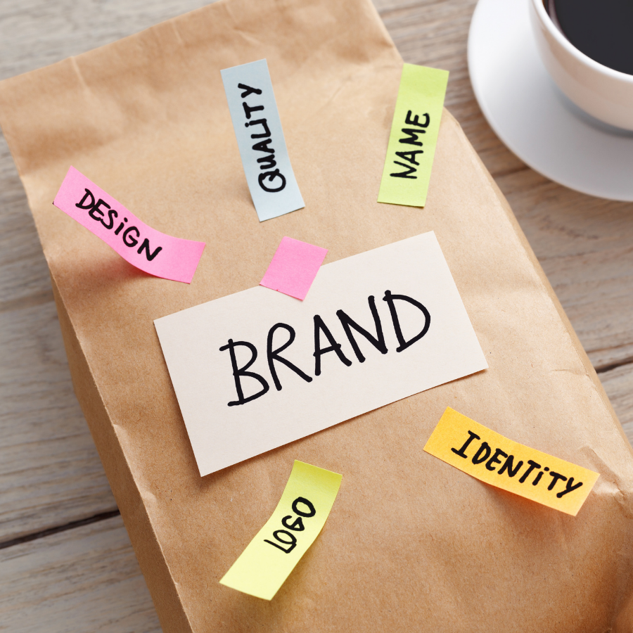 Paper bag with sticky notes labeled brand, design, quality, name, logo, and identity on a wooden table.