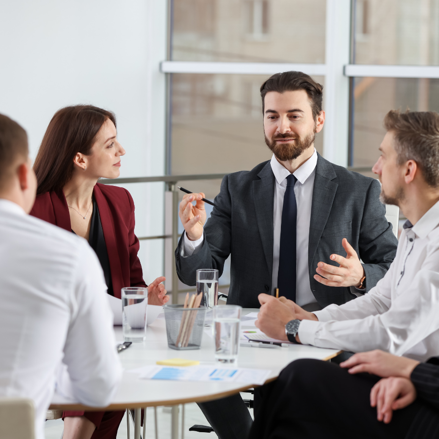 Business meeting around a table, with one man speaking and others listening attentively in an office.