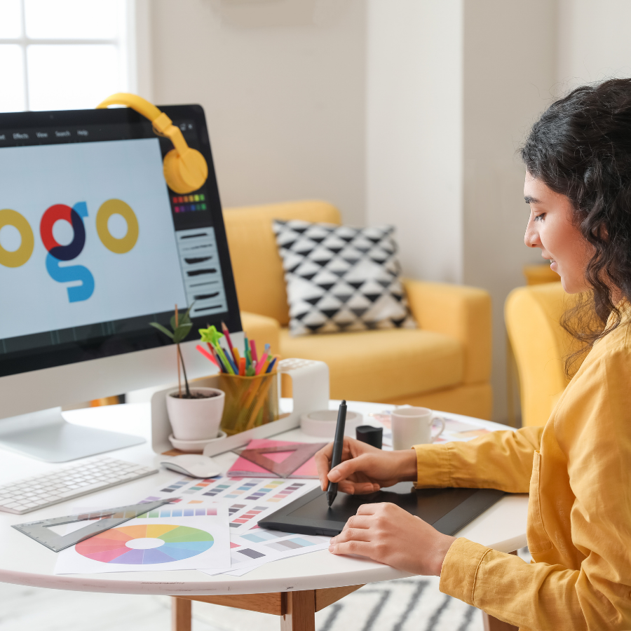 Designer sketching at a desk beside a large monitor in a bright home office