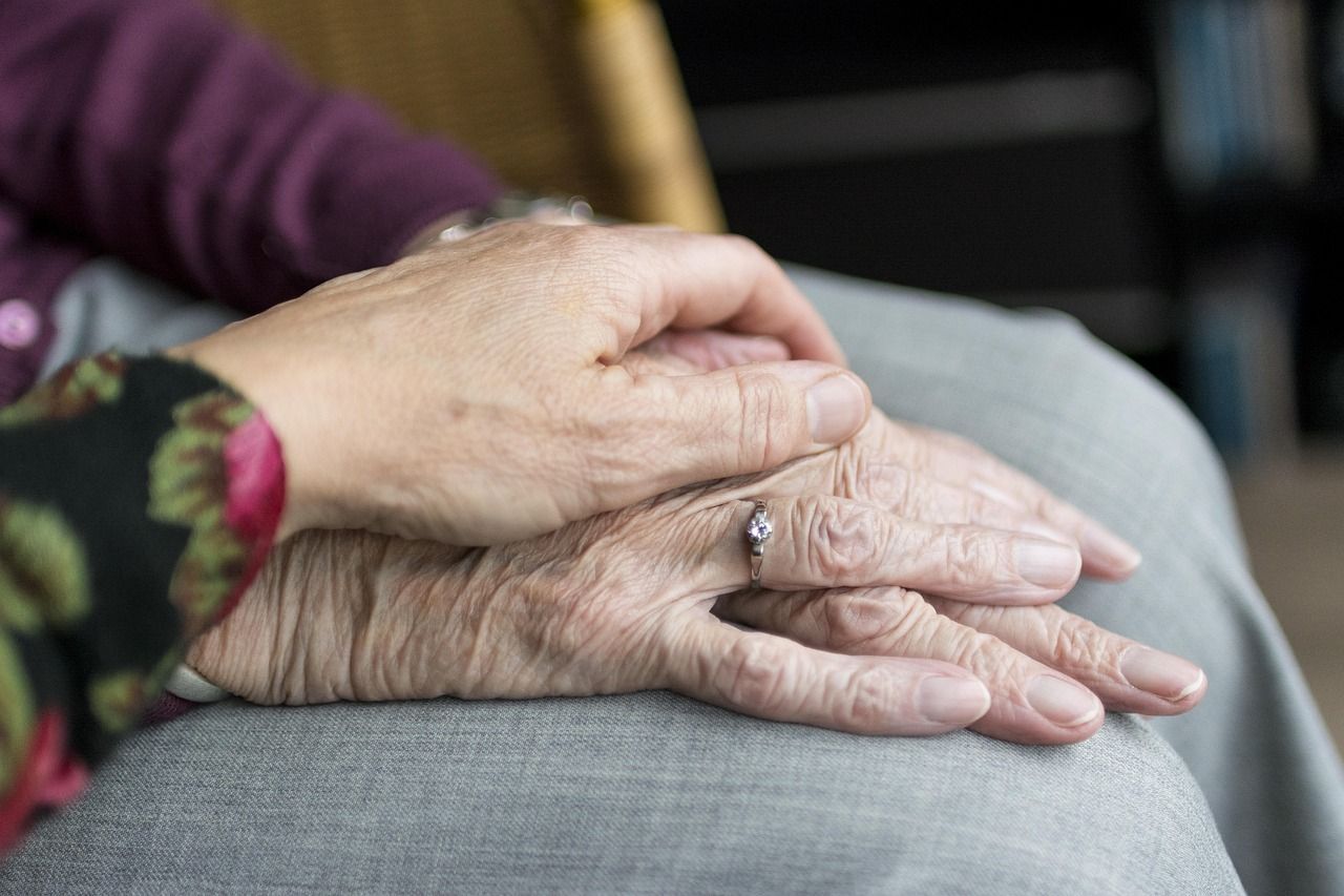 Ima of a woman with her hands laid over her legs, with another hand reaching out and holding hers
