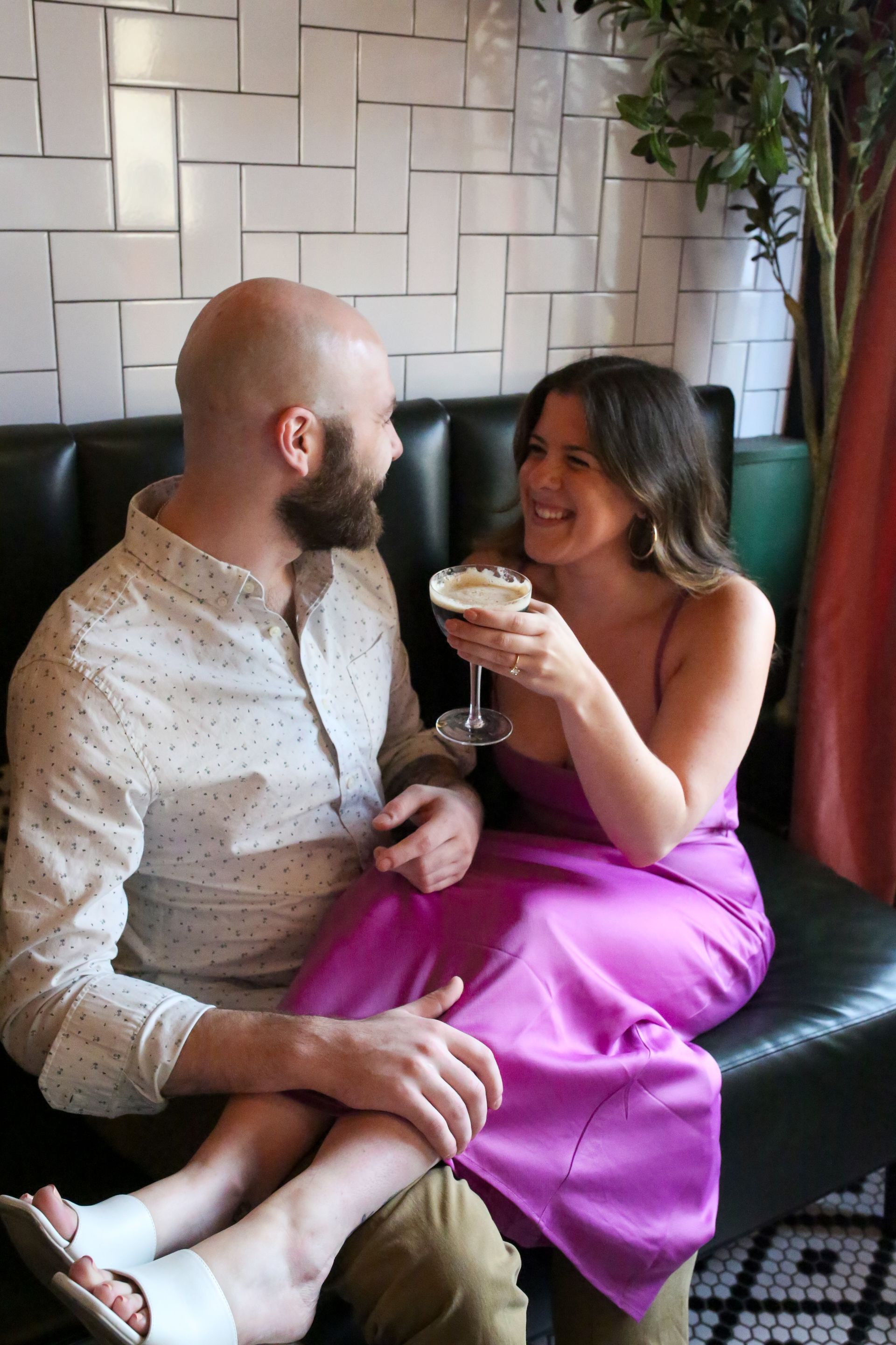 A man and a woman are sitting on a couch holding drinks.
