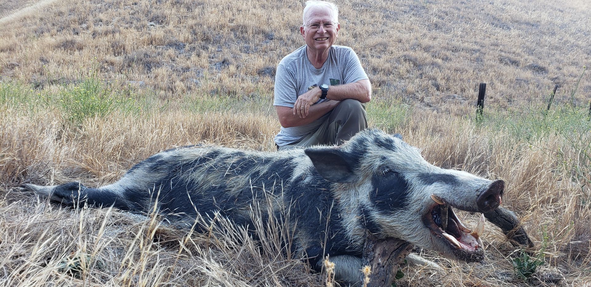 Man crouching beside a dead wild boar in a dry grass field