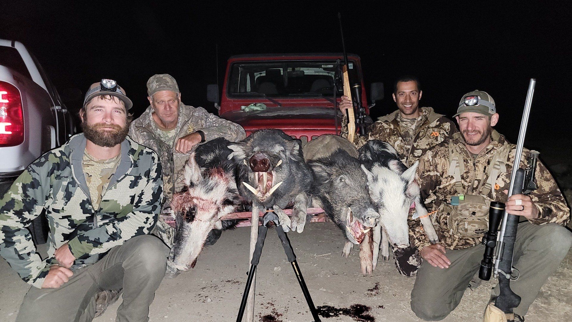 Group kneeling with two dead wild animals and rifles at night in front of a red truck
