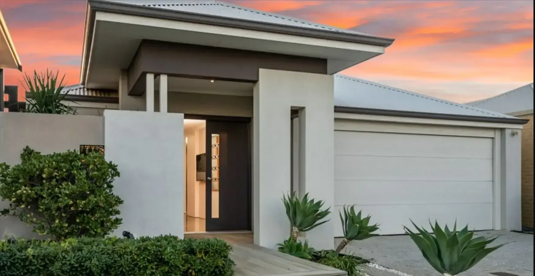 A modern house with a white garage door and a sunset in the background.