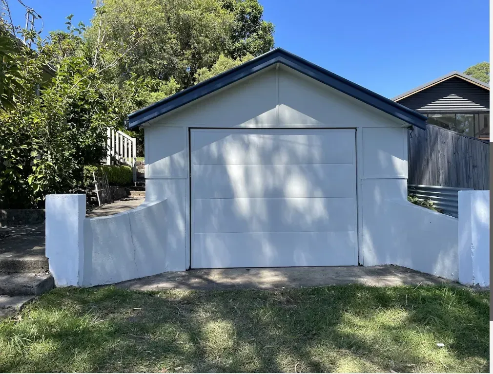 A white garage with a blue roof is in the backyard of a house.