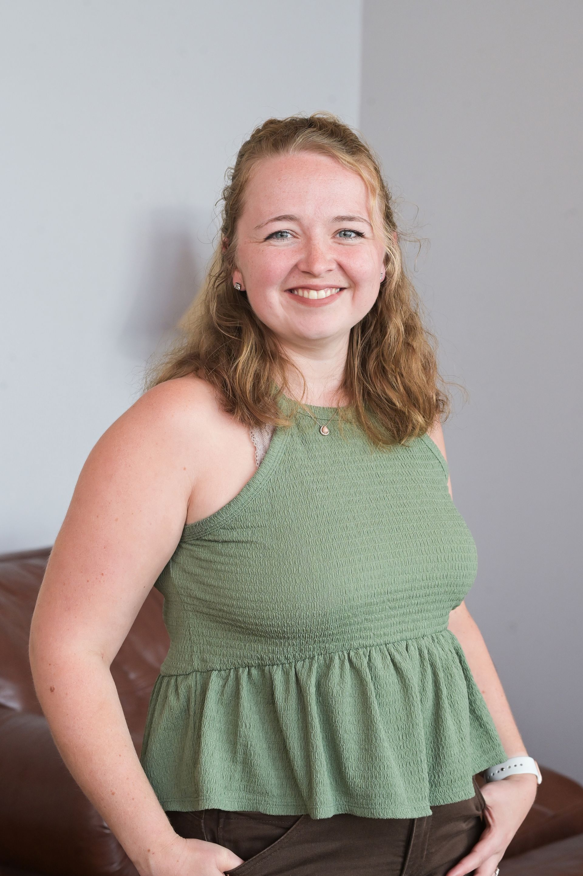 A woman in a green tank top is standing in front of a brown couch.