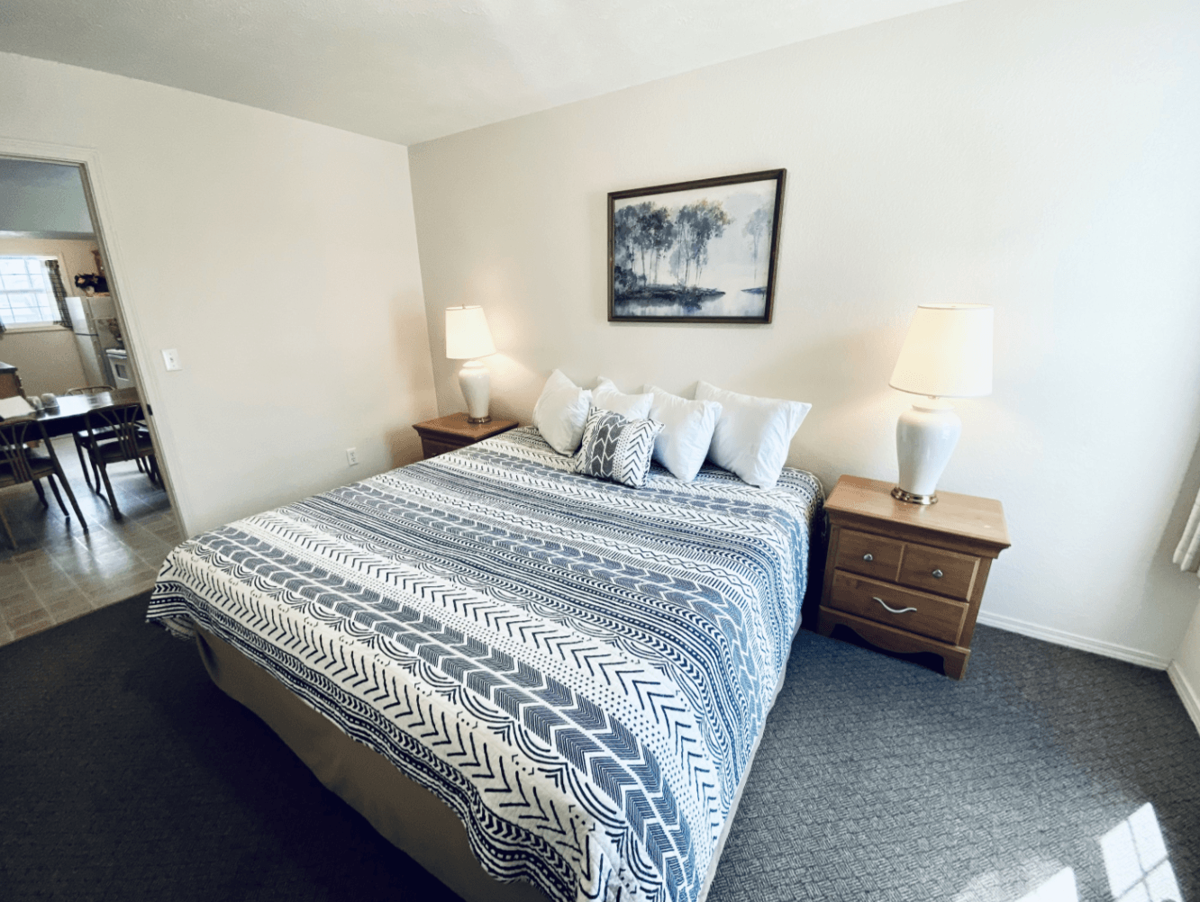 A bedroom with a king size bed , nightstands , lamps and a picture on the wall.
