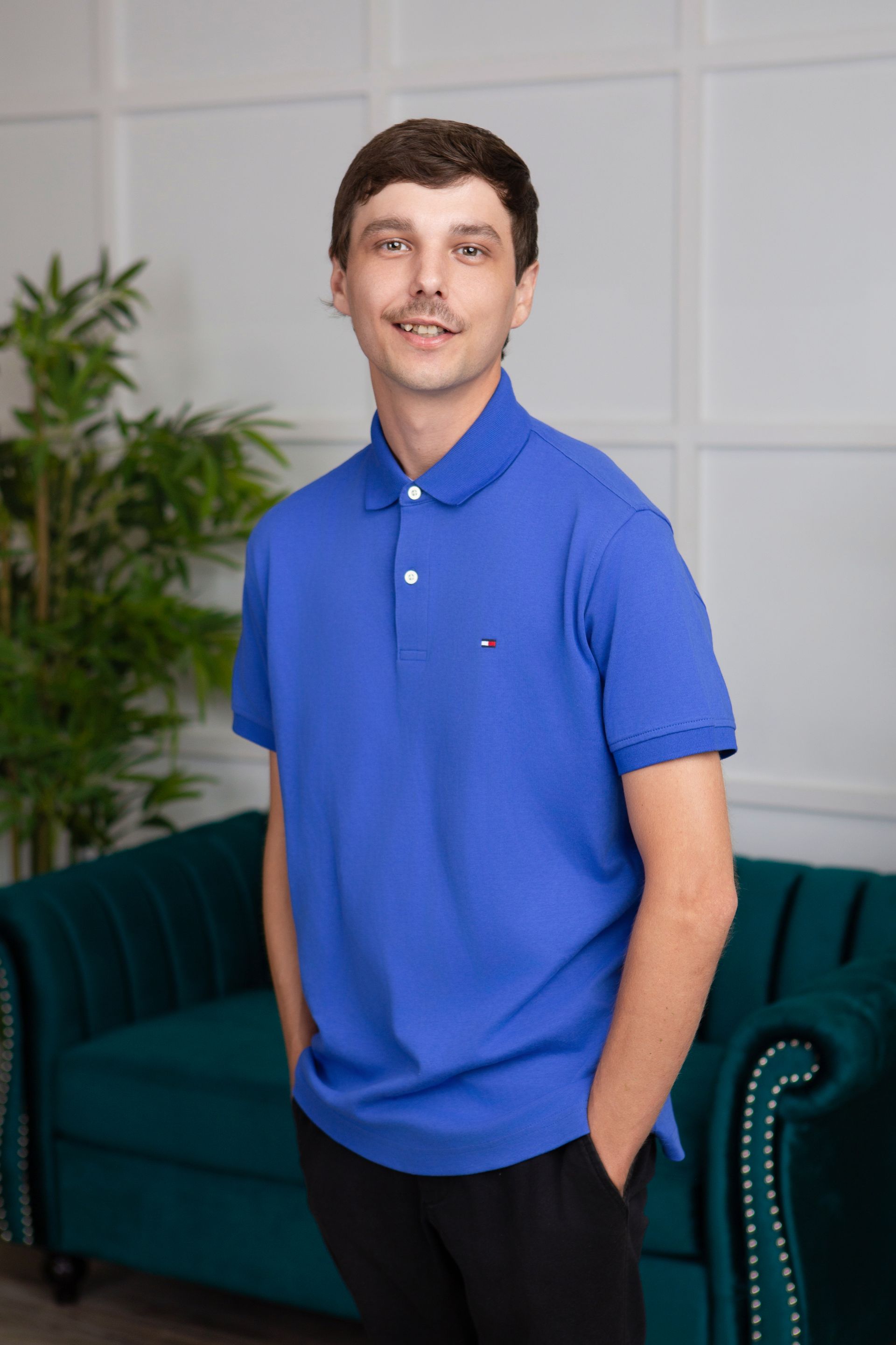 A man in a blue polo shirt is standing in front of a green couch.