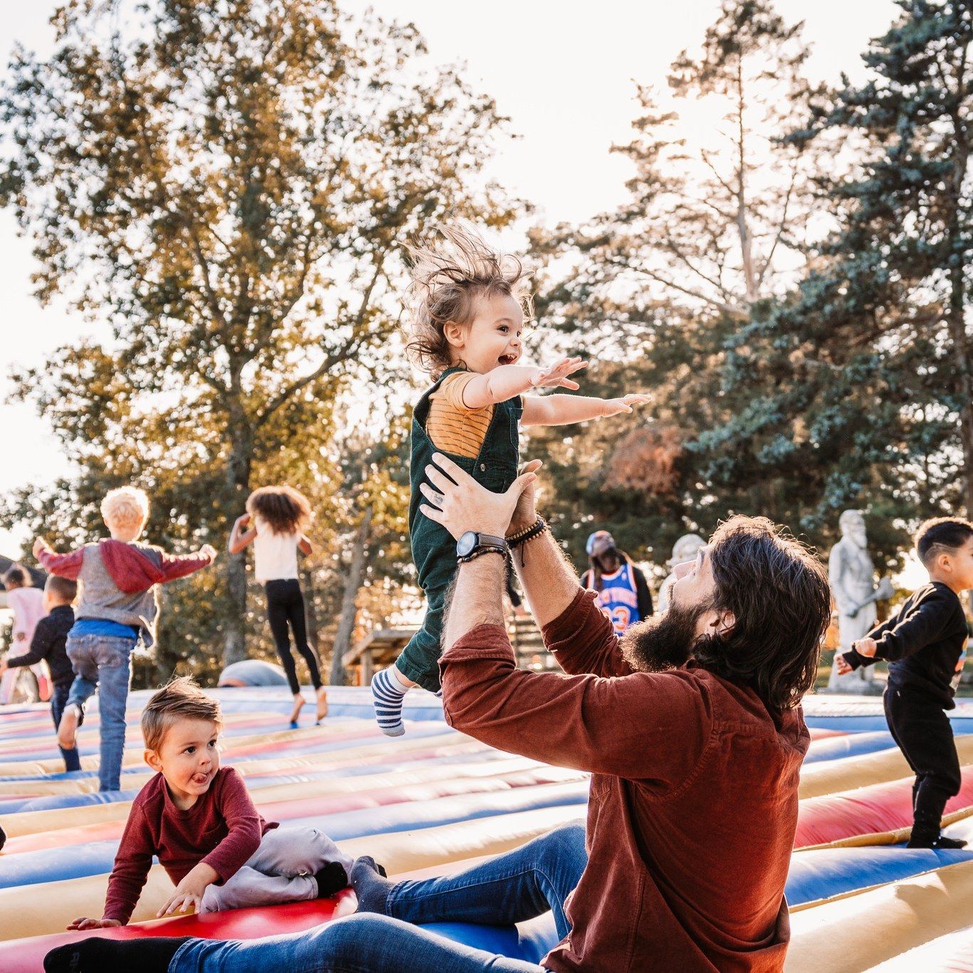A man is sitting on a trampoline holding a baby in the air.