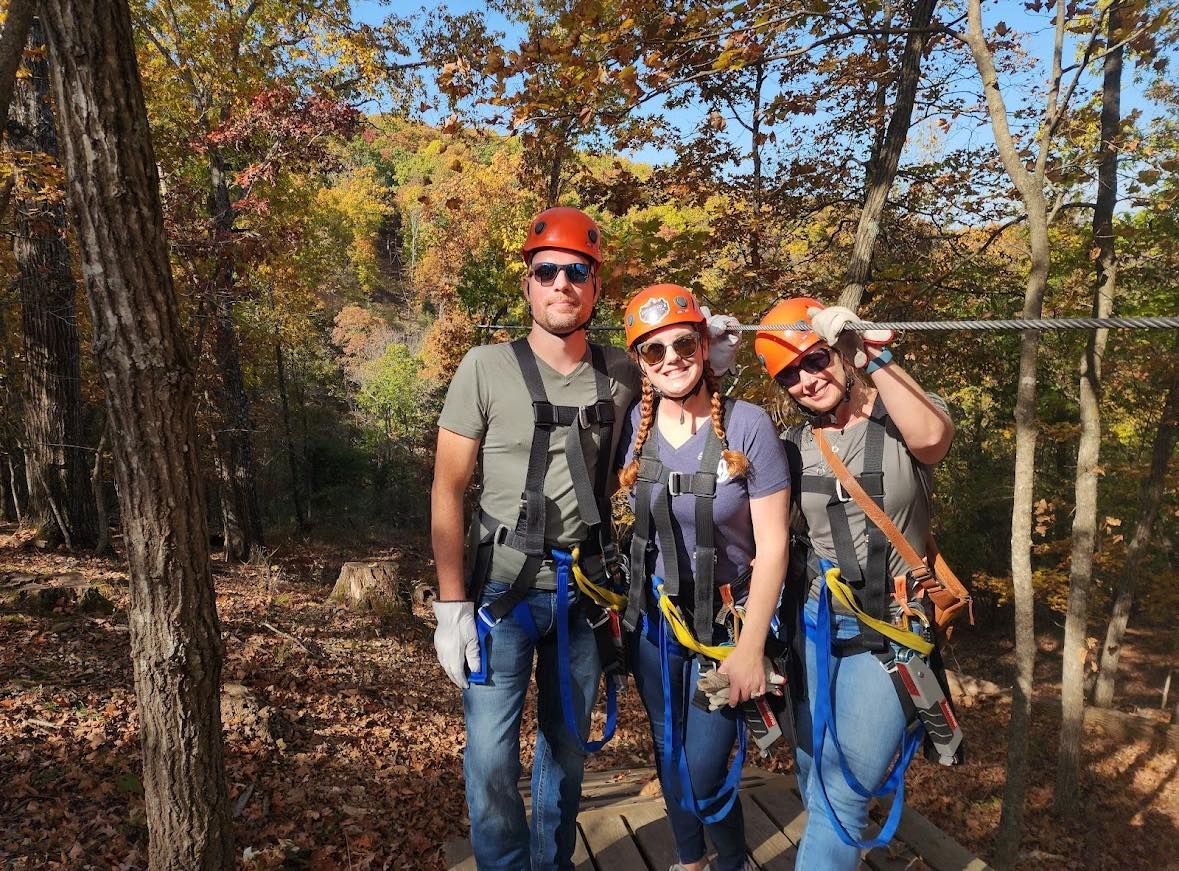 A group of people are standing next to each other on a zip line in the woods.