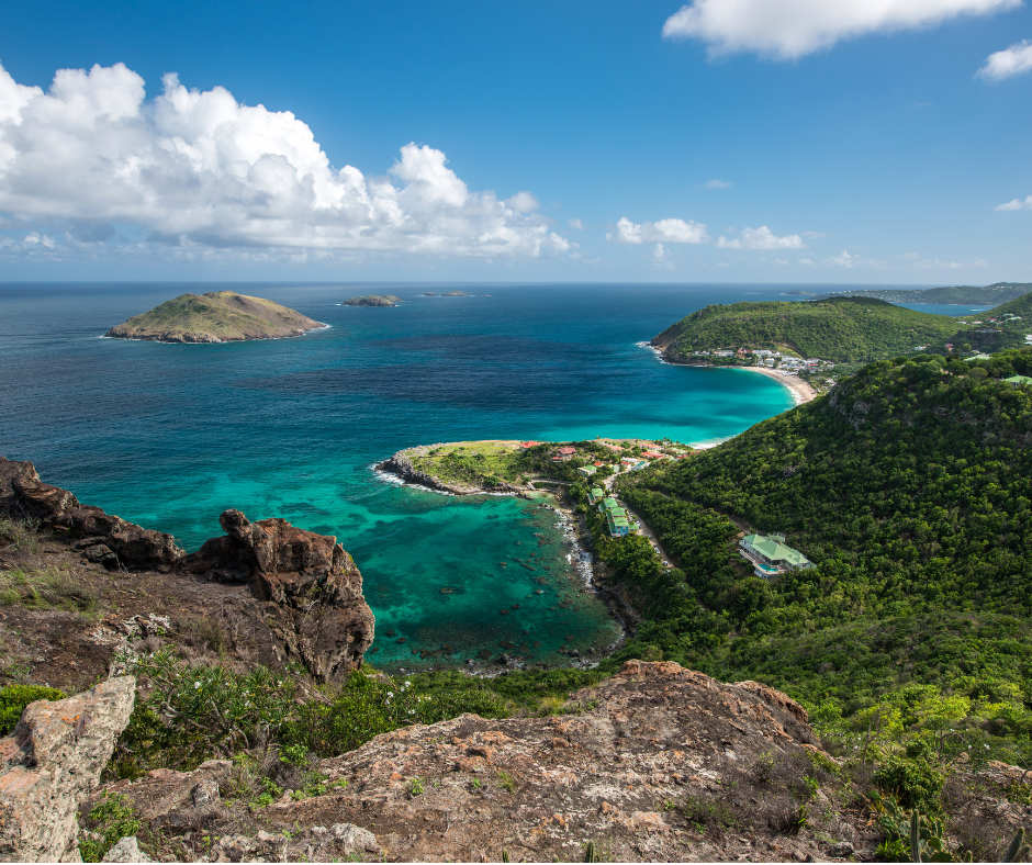 Ocean view from a high vantage point; turquoise water, green hills, blue sky with clouds.