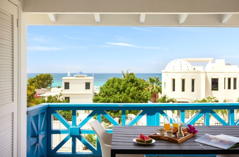 Balcony with ocean view, breakfast tray, blue railing, white building, sunny day.