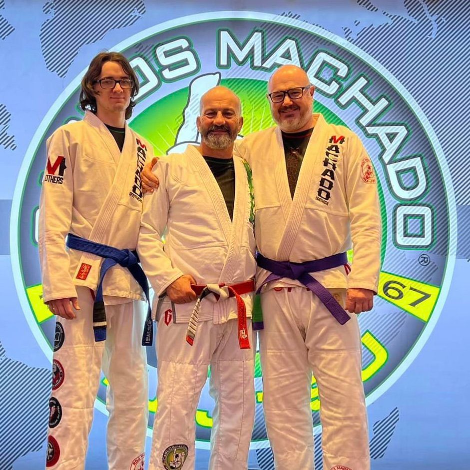 Three men are posing for a picture in front of a logo that says machado