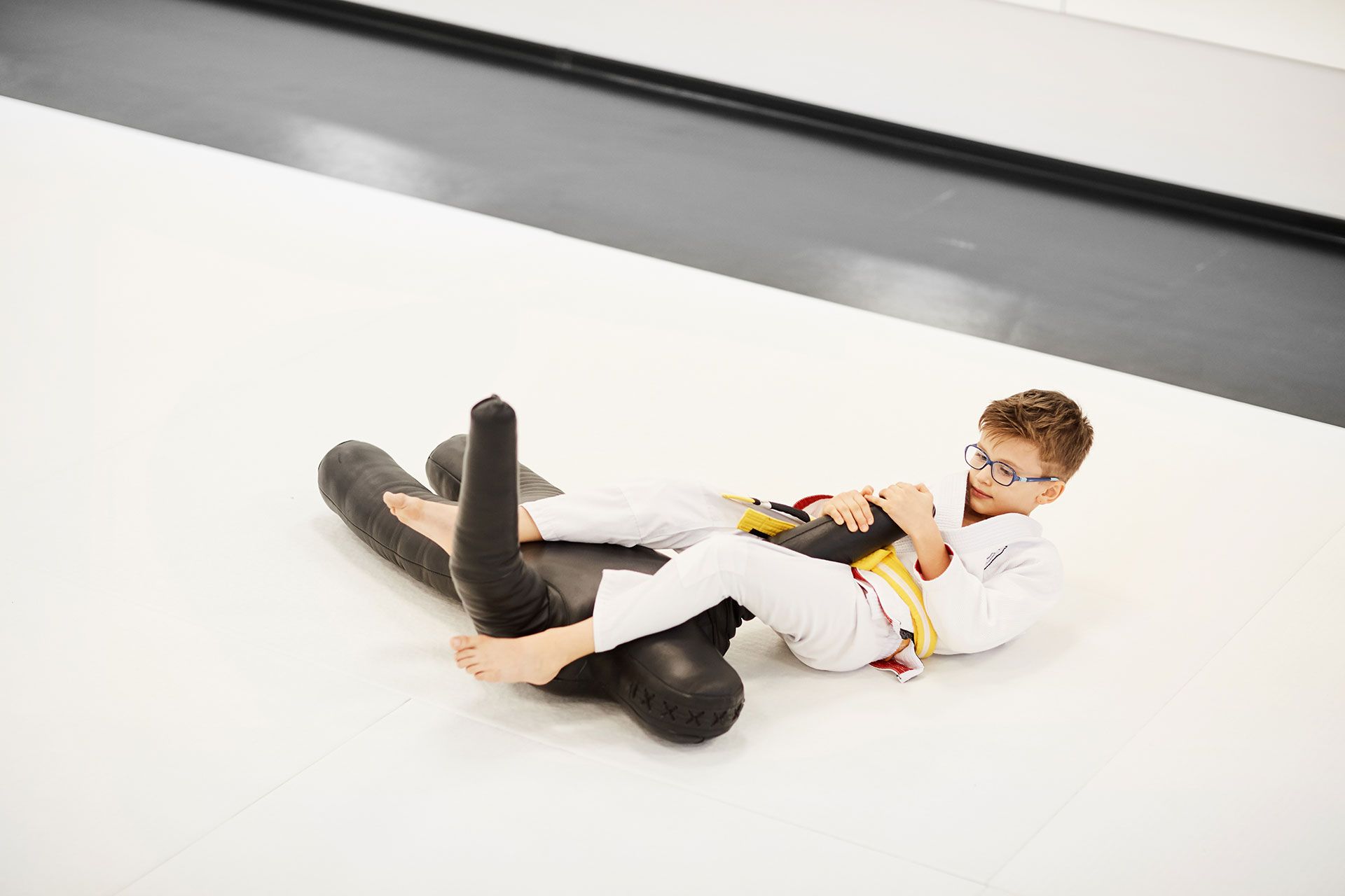 A young boy in a karate uniform is laying on the floor.