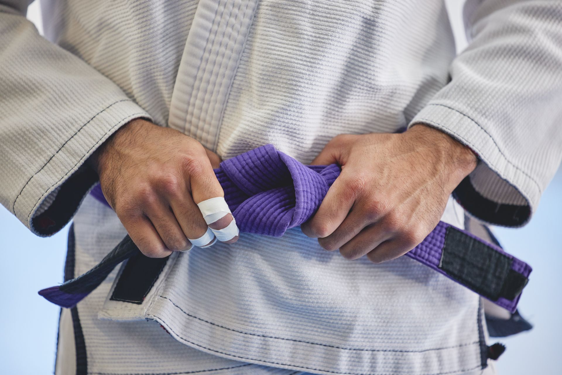 A person is tying a purple belt around their waist.