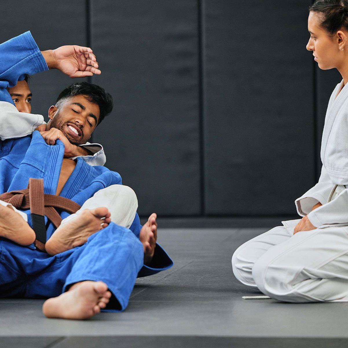 A man in a blue kimono is laying on the floor while two women watch.