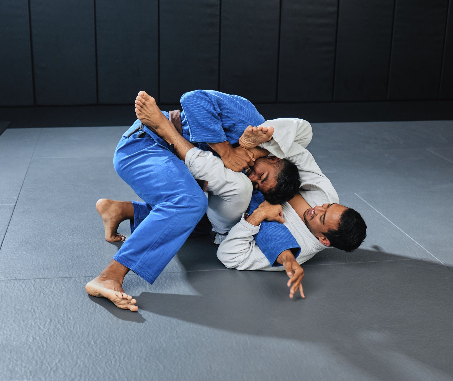 Two men are wrestling on a mat in a gym.