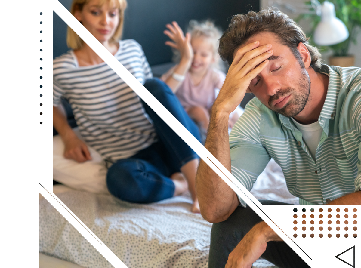 A man is sitting on a bed with his head in his hand while a woman and child are sitting on the bed.