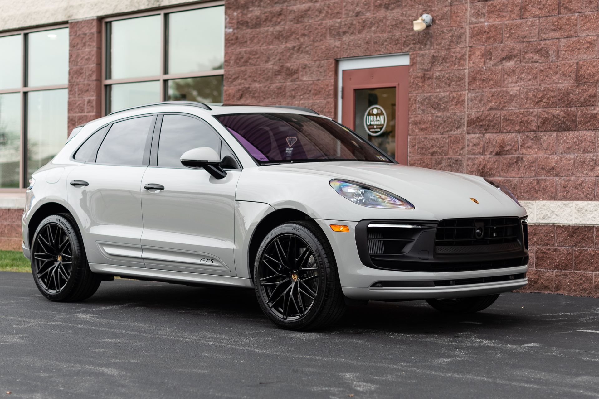 Gray Porsche Macan SUV with black wheels parked in front of a brick building.