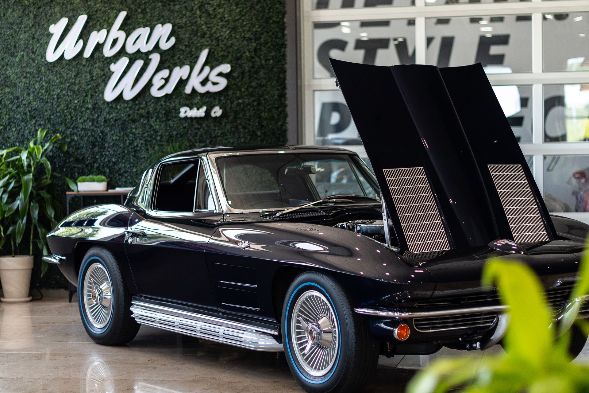 A black corvette with the hood up is parked in a showroom.