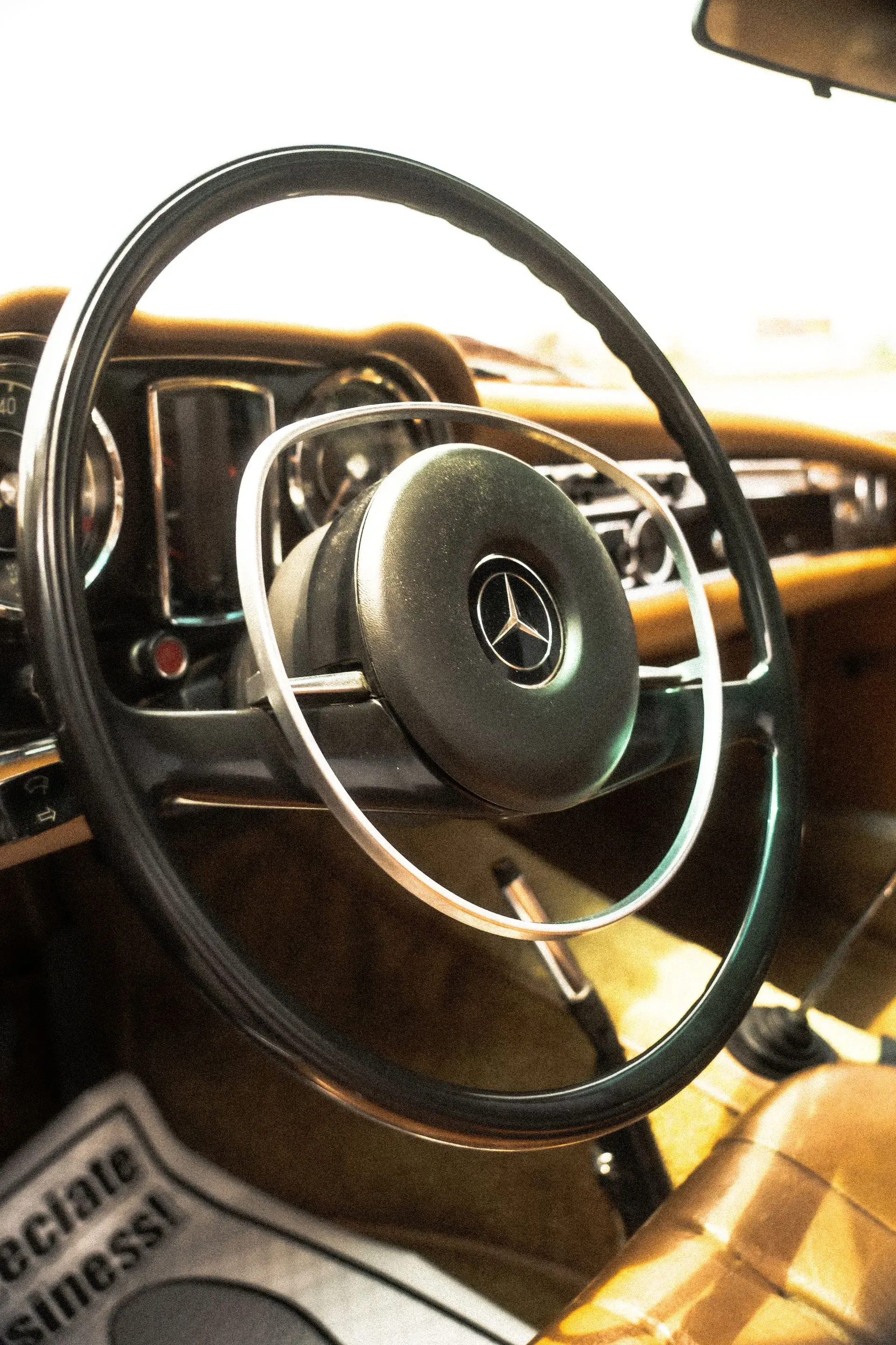 Steering wheel of a Mercedes-Benz car, with the Mercedes logo in the center. Interior is brown.