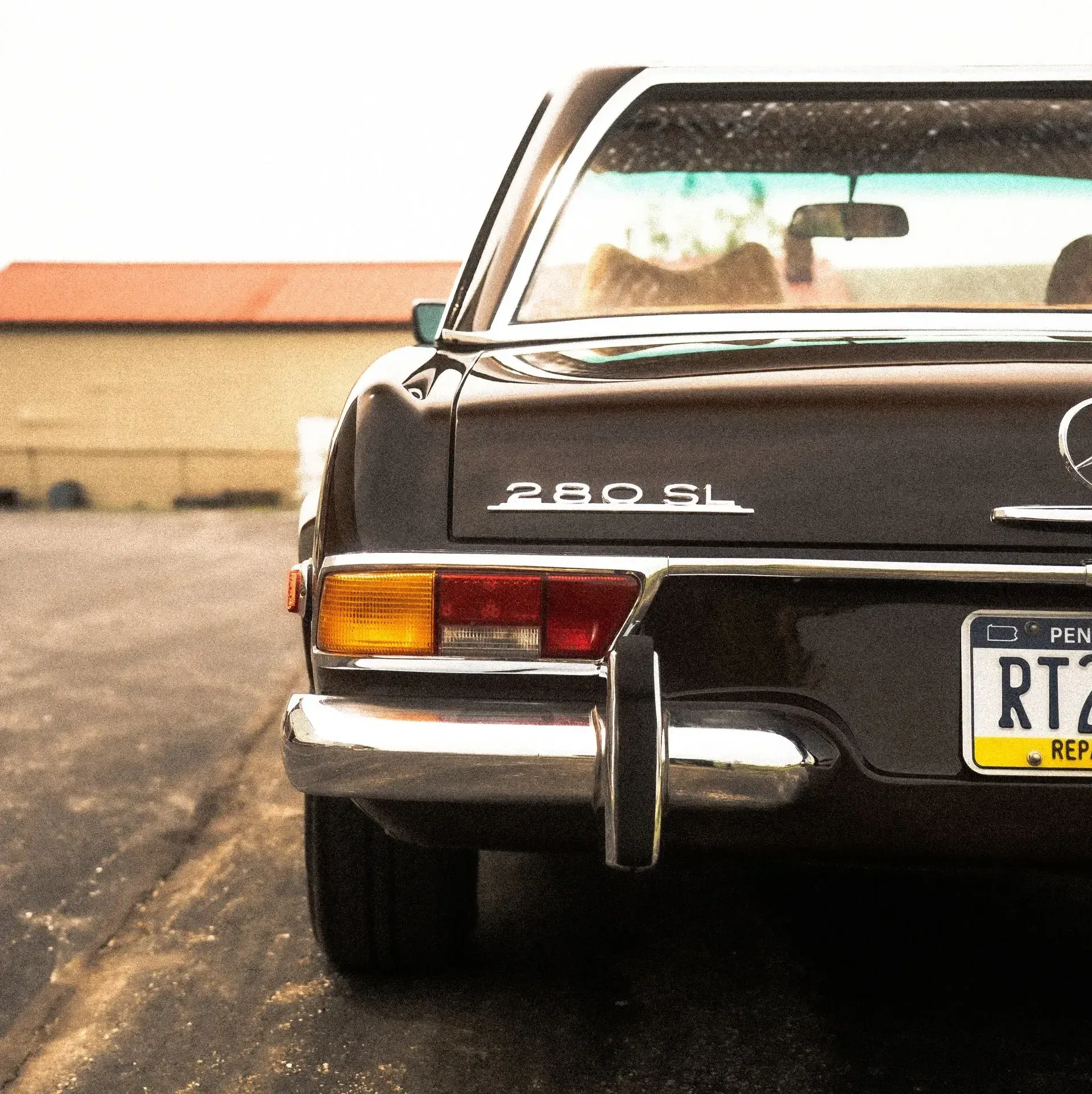 Dark brown Mercedes 280 SL parked on asphalt.  Rear view with license plate and taillights visible.
