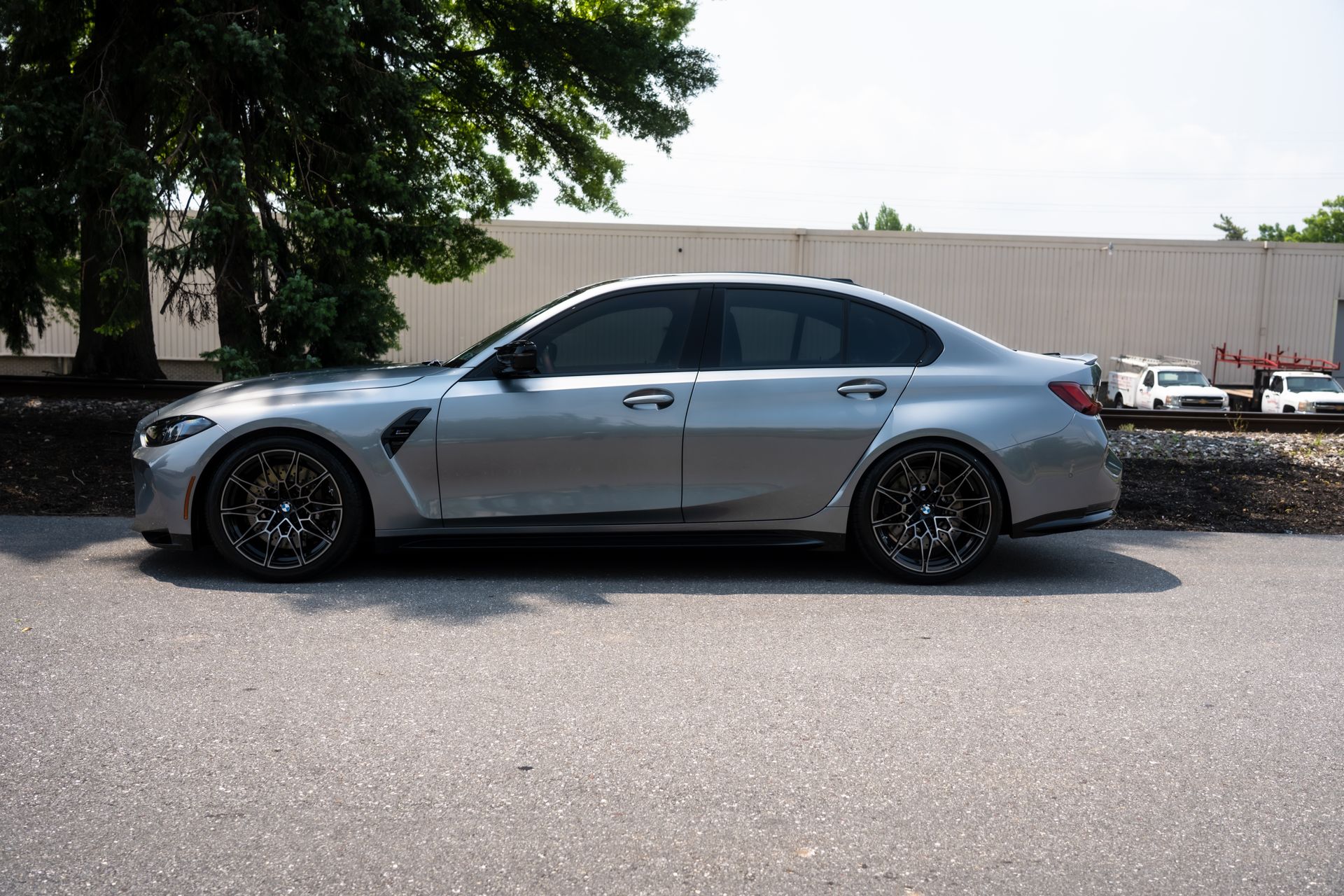 Silver BMW sedan parked on asphalt next to a building and trees.