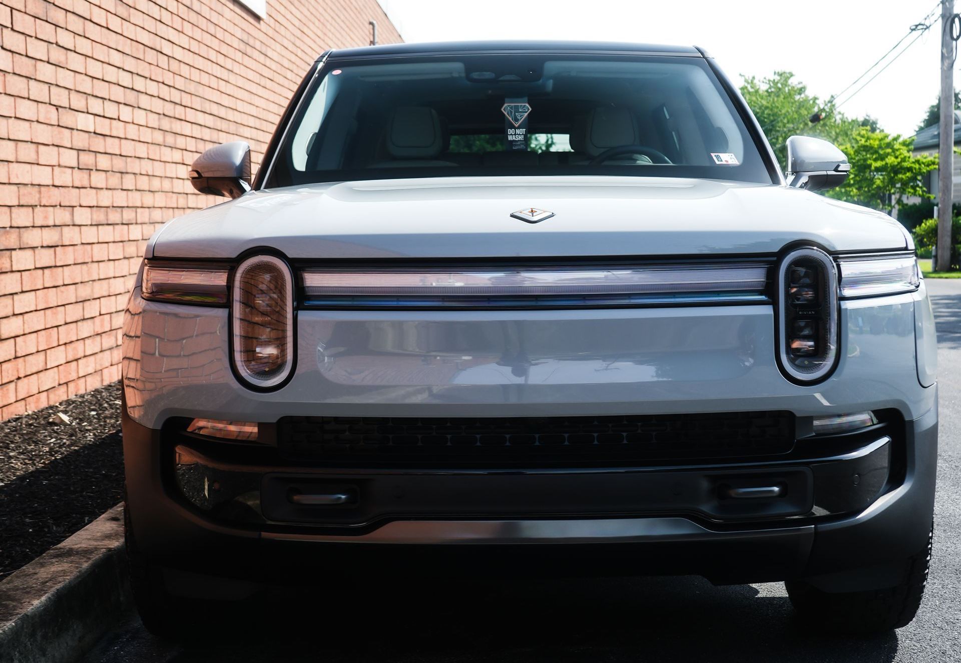 White Rivian electric SUV parked next to a brick wall.