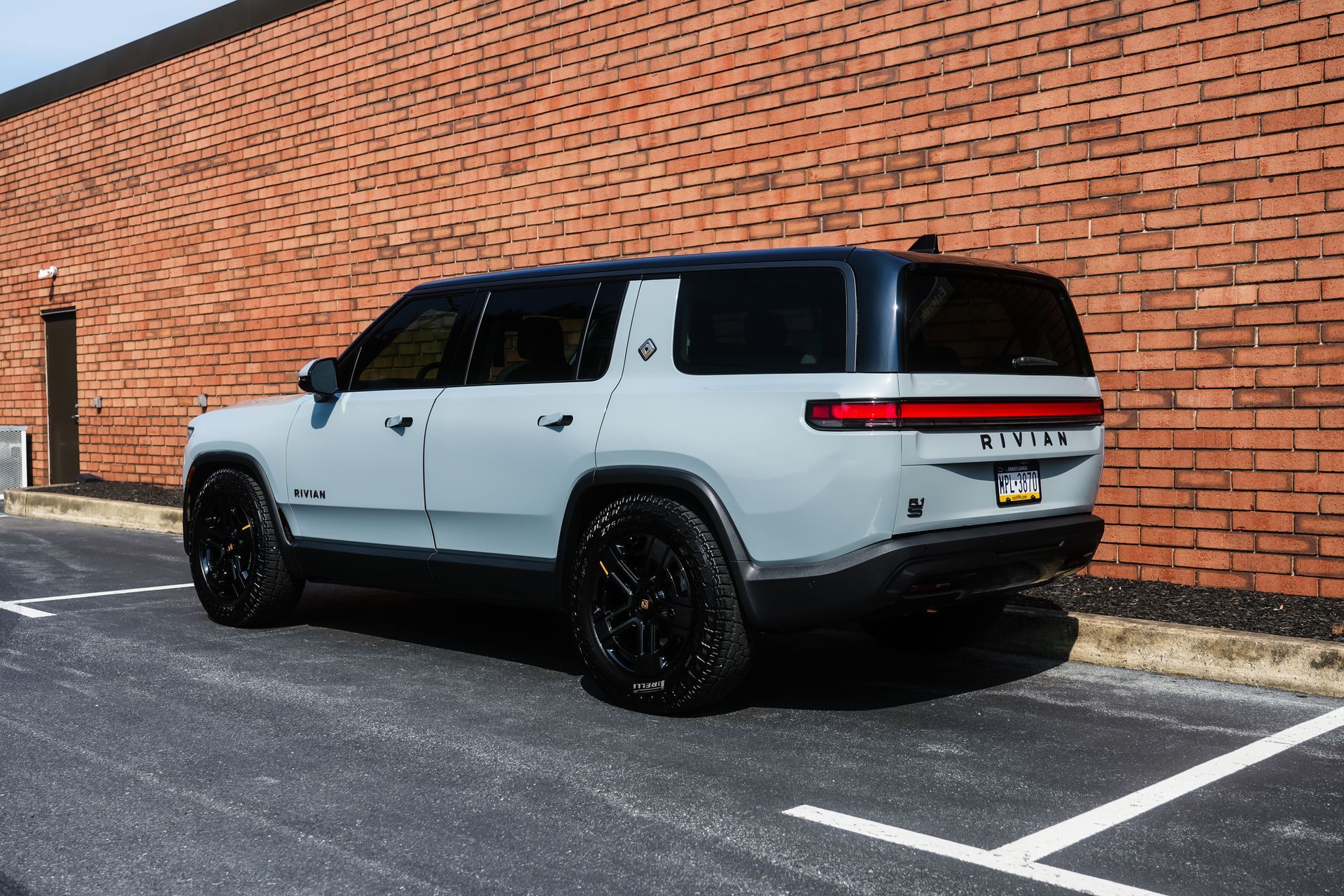Gray Rivian SUV with black accents parked in front of a brick wall.
