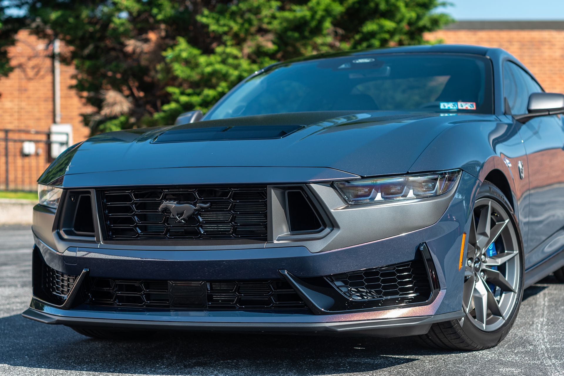 A ford mustang is parked in a parking lot in front of a brick building.