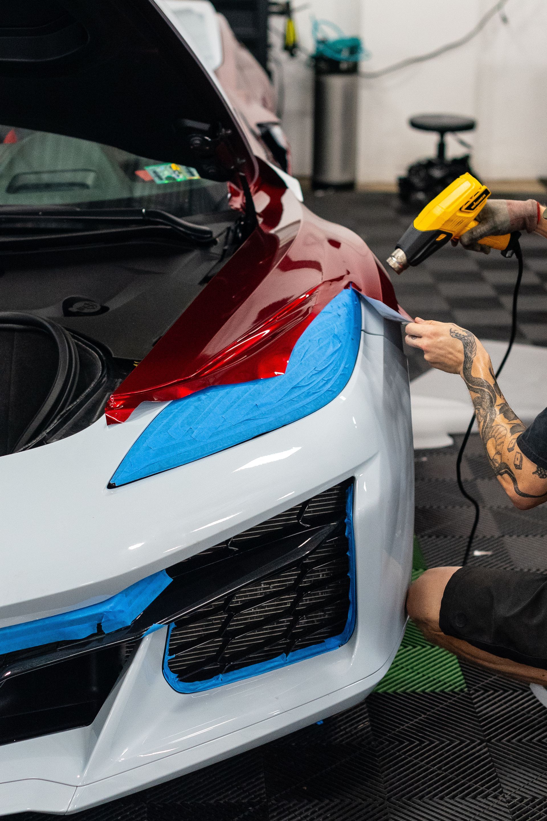 Person using a heat gun to apply film to a car's bumper, in a garage.