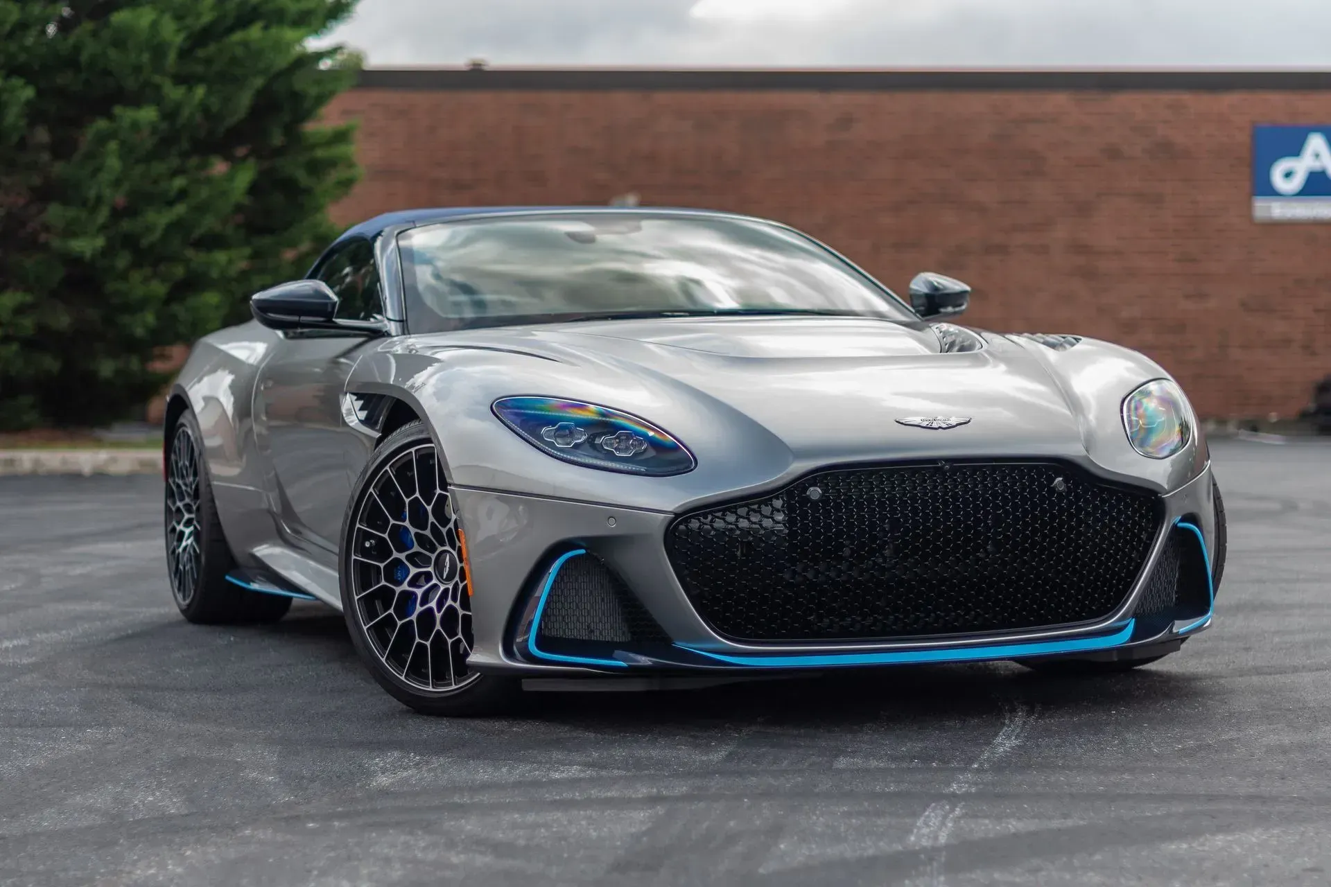 Silver Aston Martin sports car with blue accents parked on asphalt.