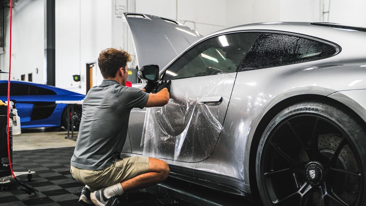 A man is wrapping a car with plastic wrap in a garage.