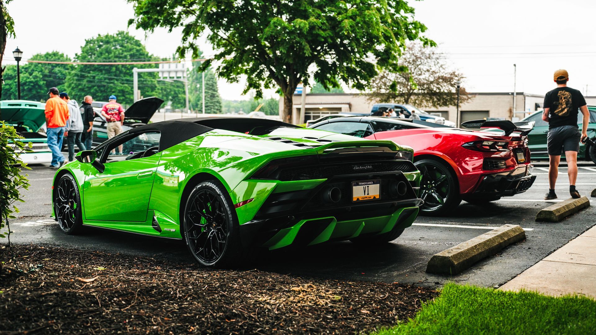 Green Lamborghini convertible and red sports car parked in lot; people nearby.