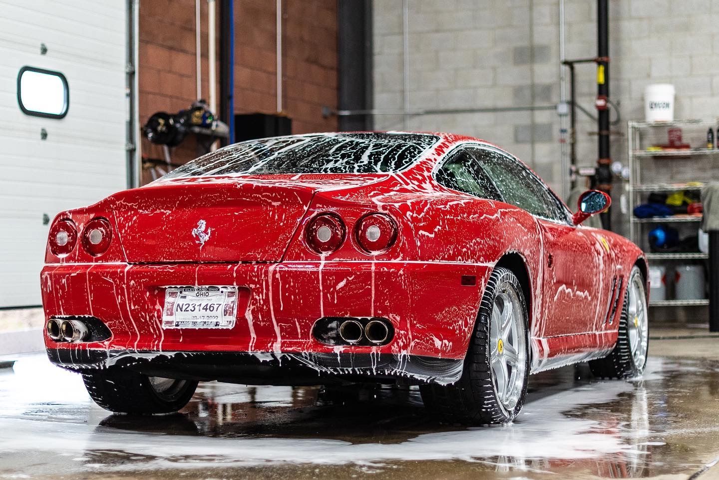 Red Ferrari being washed with foamy soap at a car wash facility.