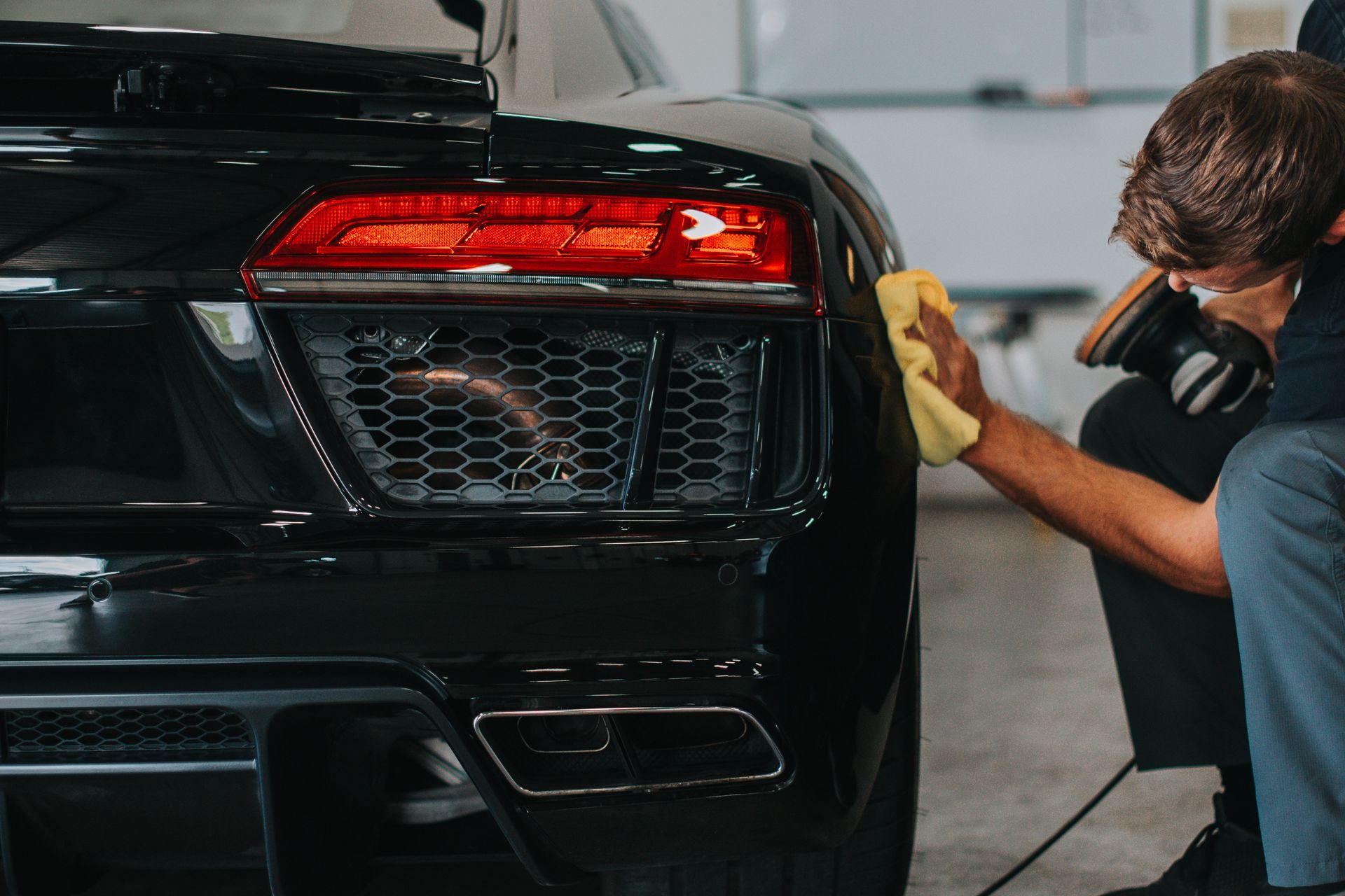 Man cleaning a shiny black sports car with a yellow cloth.