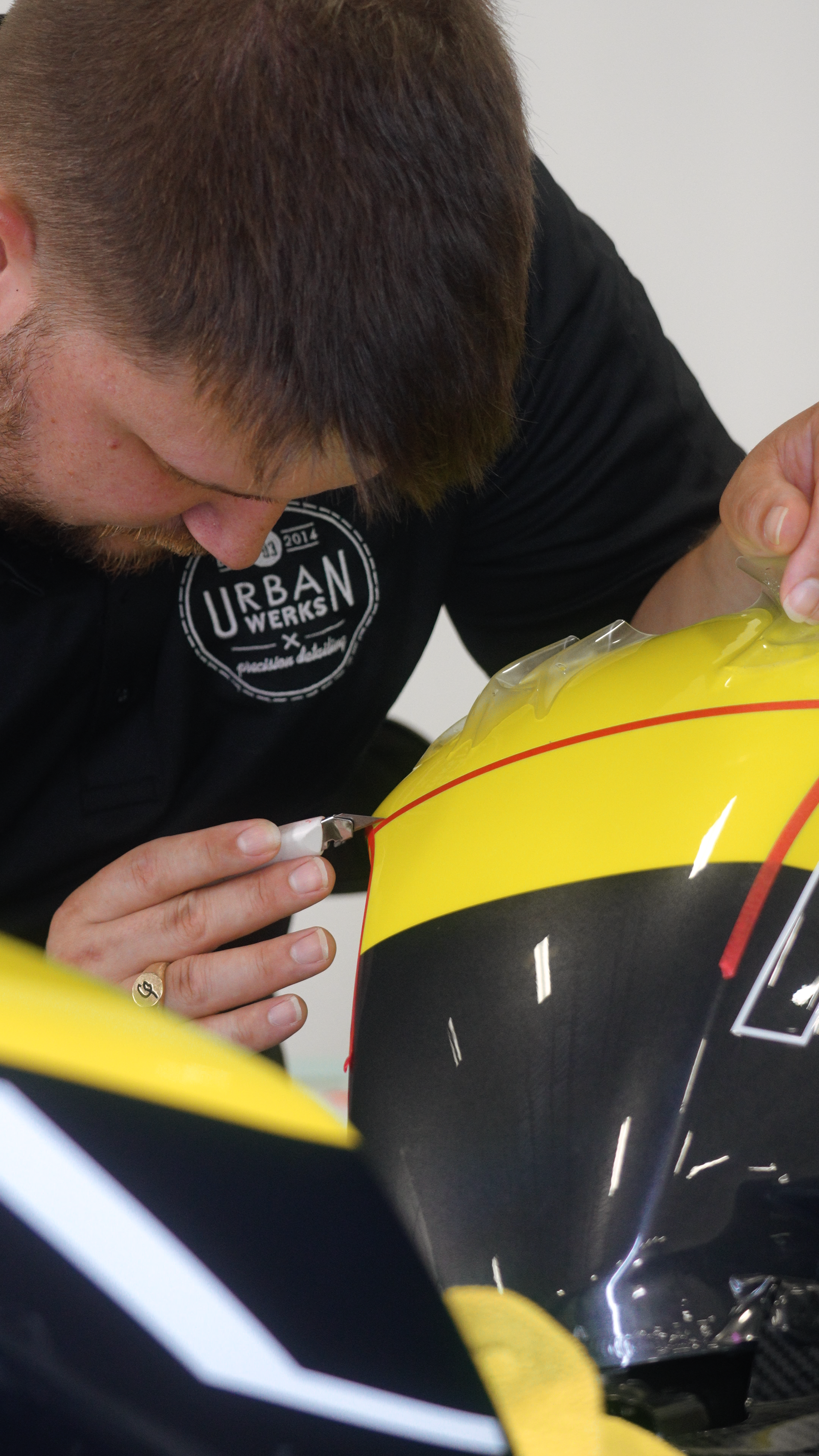 Man carefully applying decal to a yellow and black helmet, likely in a workshop.