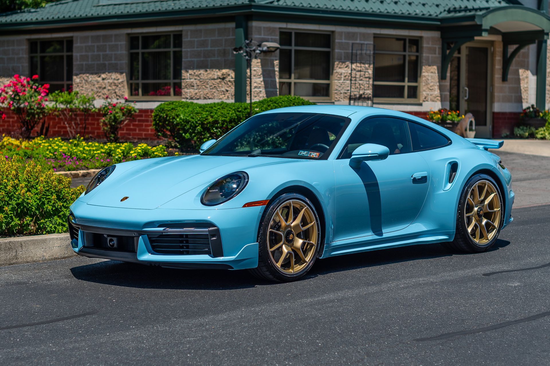 A light blue porsche 911 turbo s is parked in front of a building.
