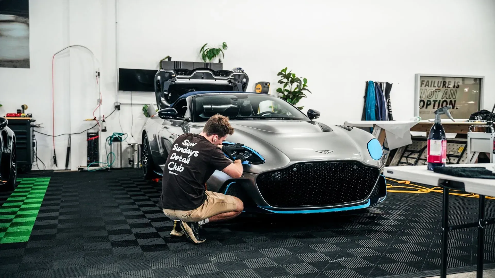 Man detailing a silver sports car in a garage with blue accents.