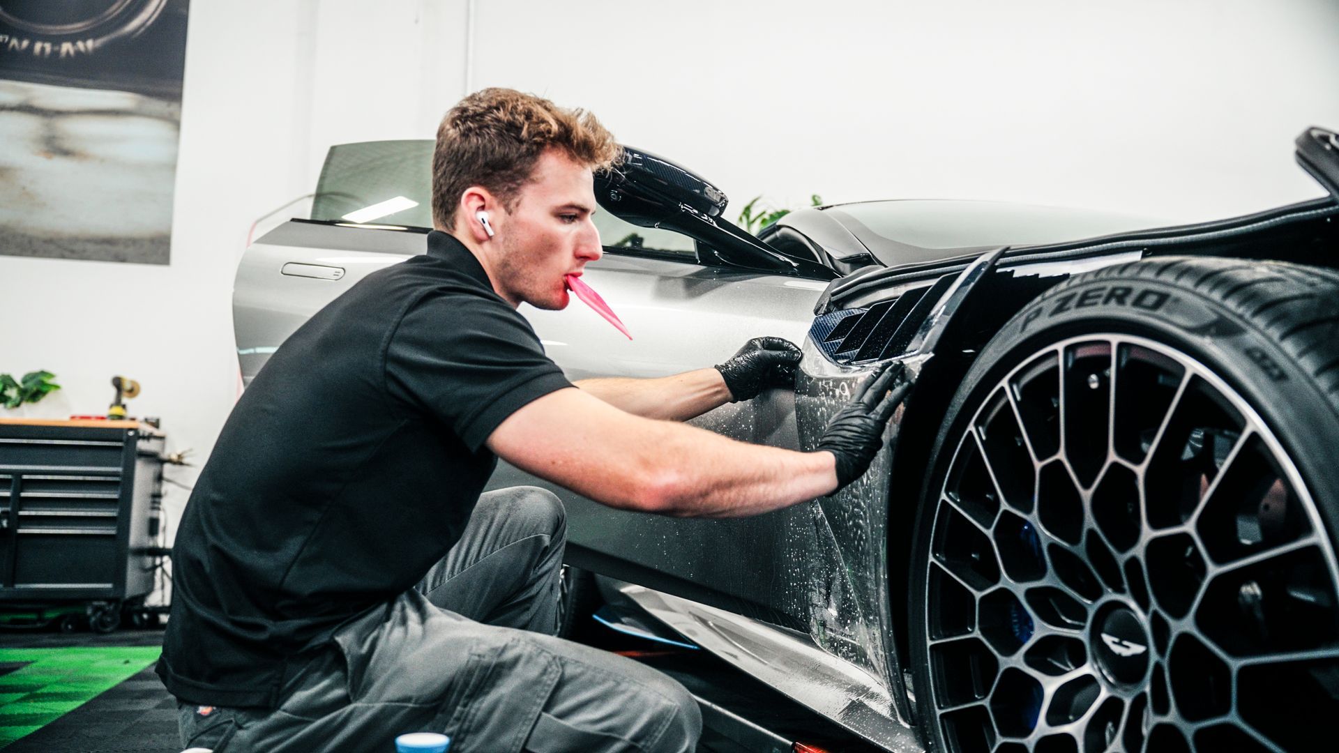 Man applying film to a car, in a garage setting, using tools.